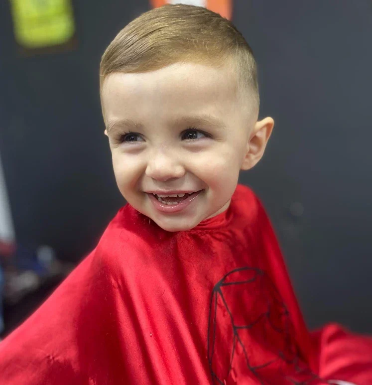 Menino sorrindo de capa vermelha depois do corte social